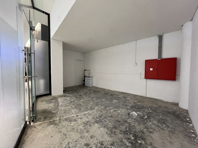 An empty utility space featuring a fire hose cabinet, a small utility sink, and exposed concrete flooring, accessible via a glass entrance door.