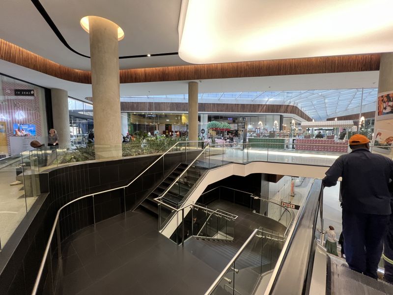 Modern multi-level retail mall interior featuring a central staircase, glass balustrades, and contemporary architectural lighting design.