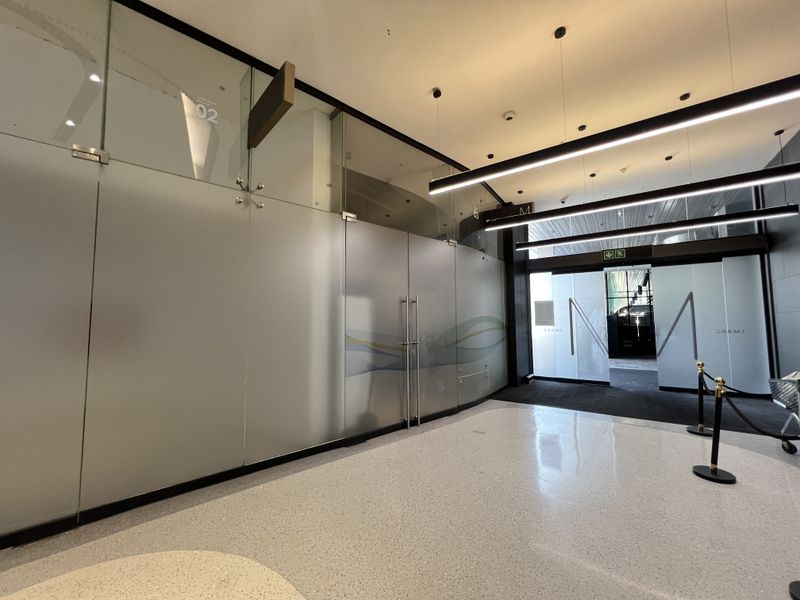 Modern commercial entrance lobby featuring polished terrazzo flooring, sleek linear pendant lighting, and contemporary frosted glass partition walls.