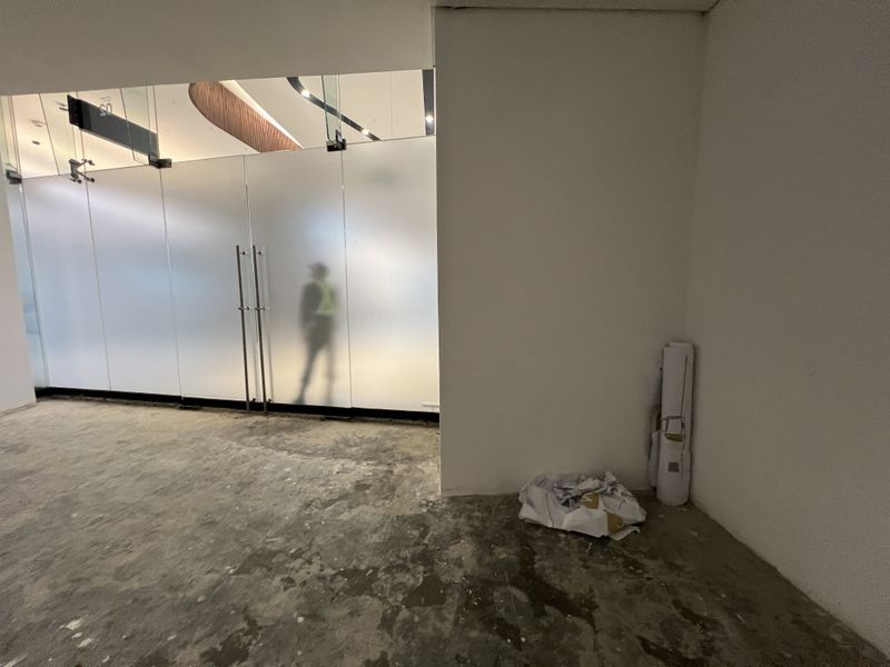 An unfinished commercial entry space featuring a frosted glass partition, recessed lighting, and a timber ceiling detail, currently awaiting final flooring installation.