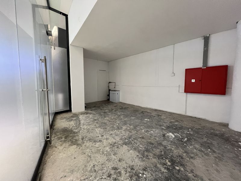 An empty utility or storage space featuring a fire hose cabinet, a small utility sink, and unfinished concrete flooring with a glass partition wall.