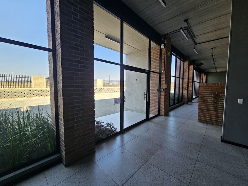 Modern industrial hallway featuring exposed brick columns, large glass windows, polished tiled flooring, and an exposed concrete ceiling with track lighting.