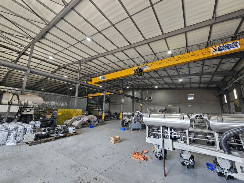 Spacious industrial warehouse facility featuring high ceilings, concrete flooring, and an integrated overhead bridge crane system suitable for heavy manufacturing or storage operations.