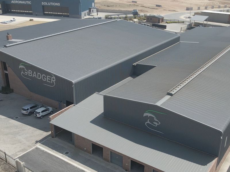 Aerial view of a large industrial facility featuring extensive corrugated metal roofing, brick exterior walls, and multiple roller shutter access points.