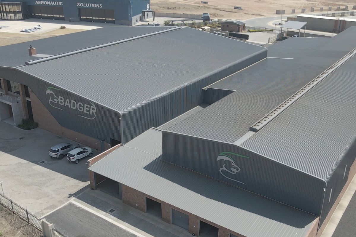 Aerial view of a large industrial facility featuring extensive corrugated metal roofing, brick exterior walls, and multiple roller shutter access points.