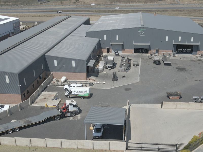 Aerial view of an industrial property featuring large warehouse buildings, extensive asphalt yard space, perimeter walling, and covered parking facilities.