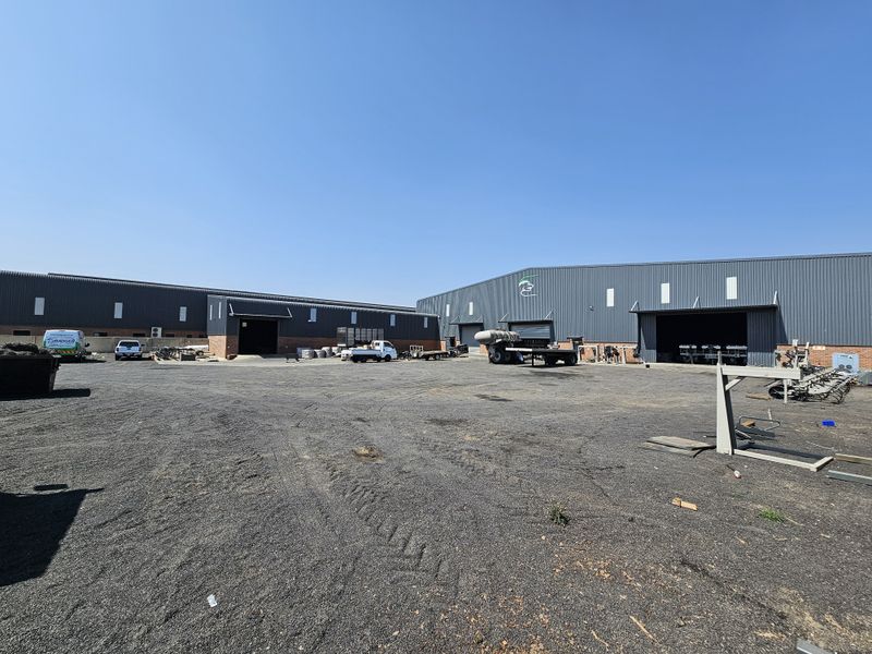 Spacious industrial yard area featuring large metal-clad warehouse buildings with multiple roller shutter access points and ample open space for logistics or storage.