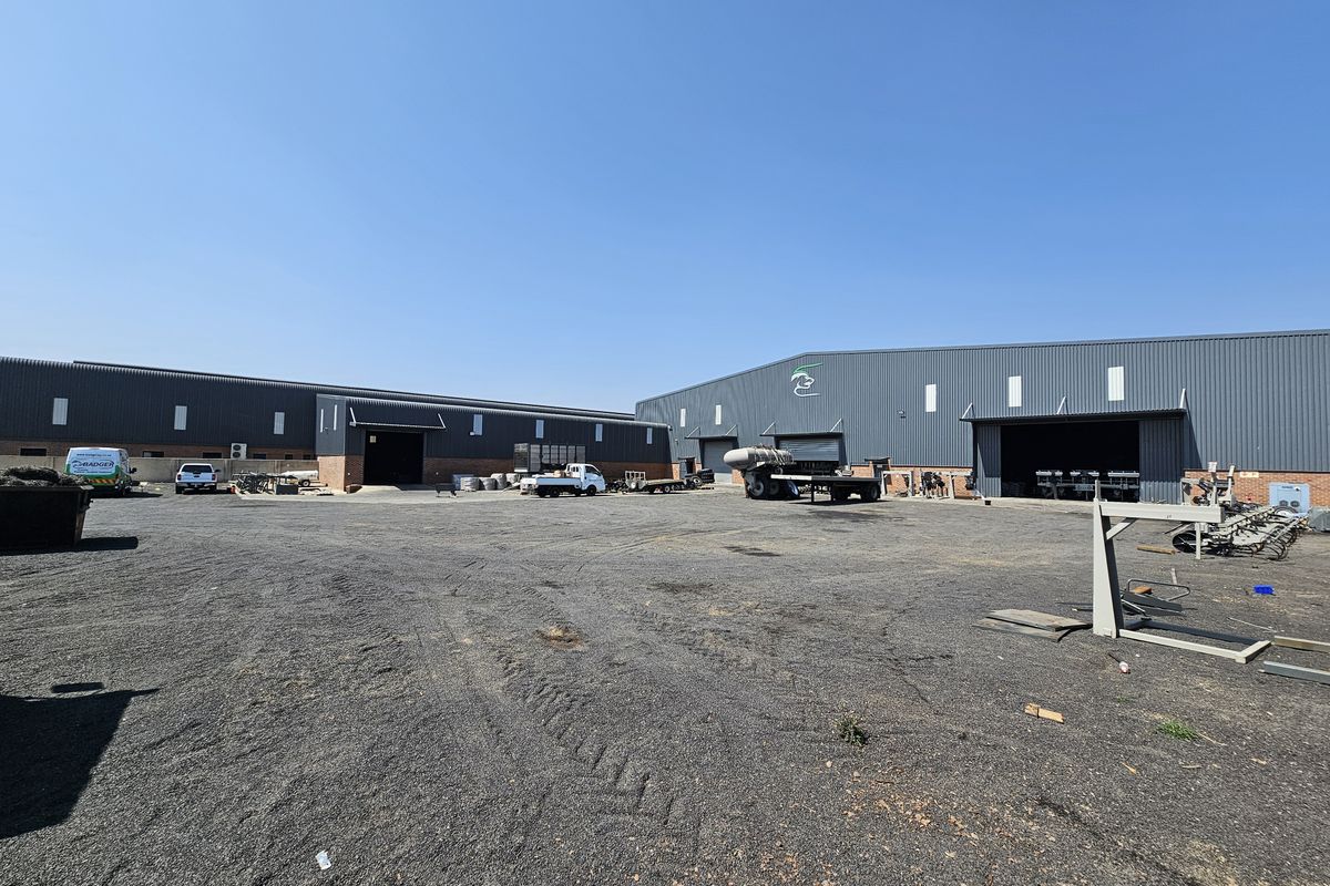 Spacious industrial yard area featuring large metal-clad warehouse buildings with multiple roller shutter access points and ample open space for logistics or storage.