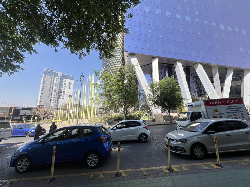 Exterior view of a modern commercial building featuring a glass facade and structural columns, situated in a busy urban environment.