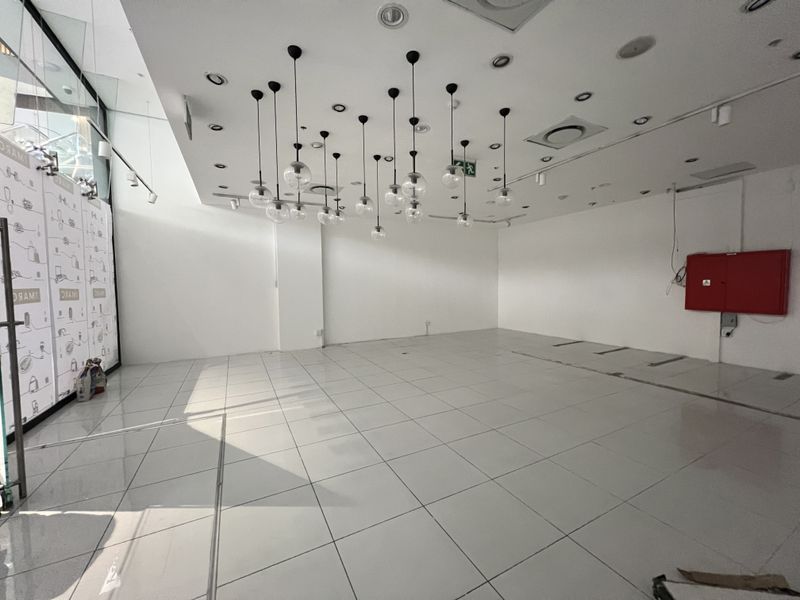 An empty, open-plan retail space featuring tiled flooring, modern pendant lighting, and a large glass storefront, suitable for various commercial uses.