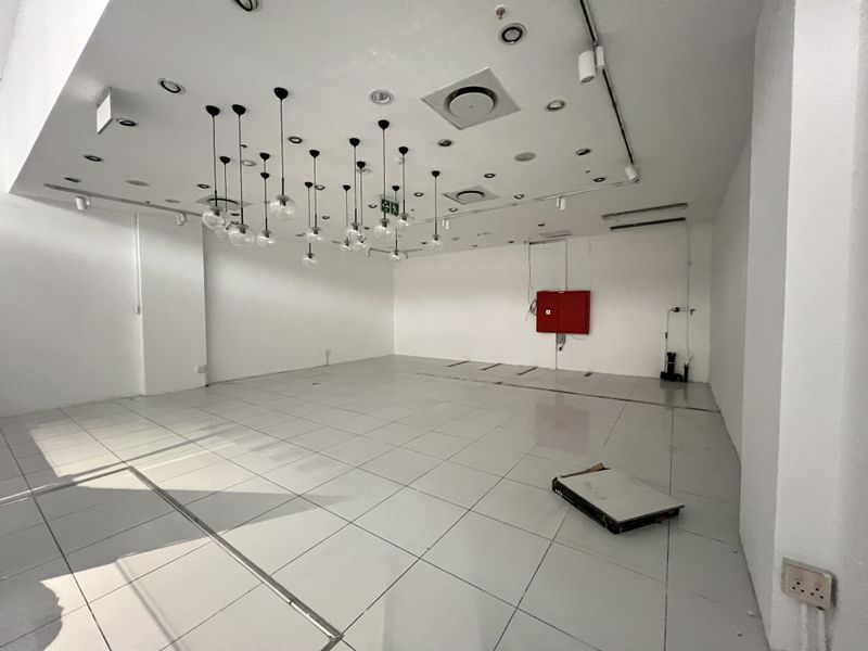 A spacious, empty retail unit featuring white tiled floors, modern pendant lighting, and integrated ceiling air conditioning vents.