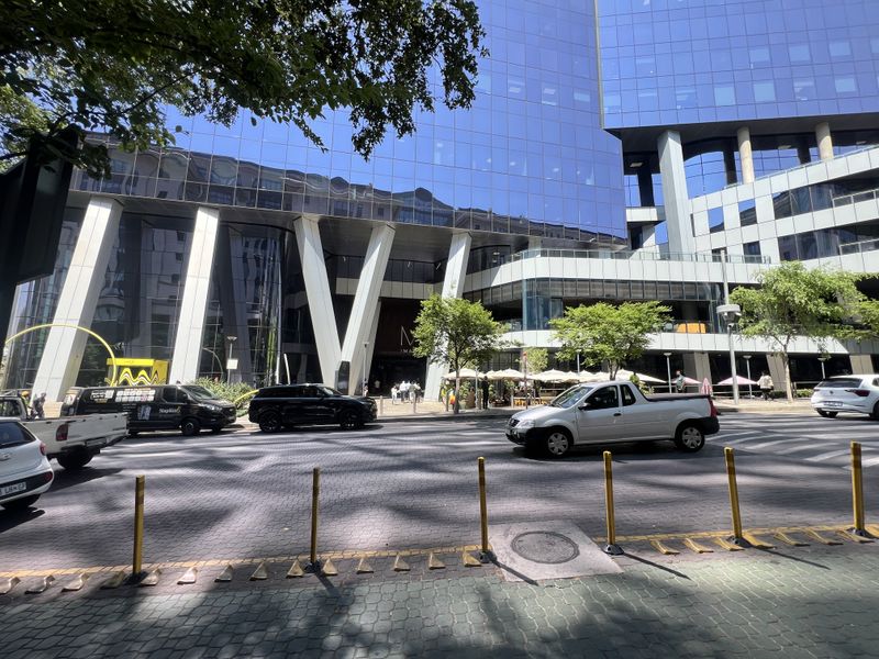 Street-level view of a modern commercial building featuring a prominent glass facade and structural architectural columns.
