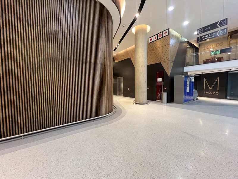 Modern commercial building lobby featuring high-end timber slat wall cladding, polished terrazzo flooring, and architectural concrete columns with clear directional signage.
