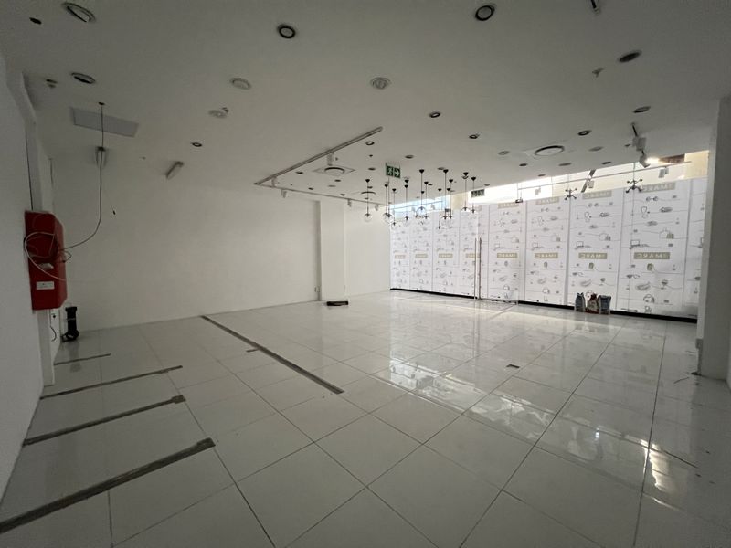 An empty open-plan retail space featuring tiled flooring, recessed lighting, and a large glass storefront, currently in a shell condition.