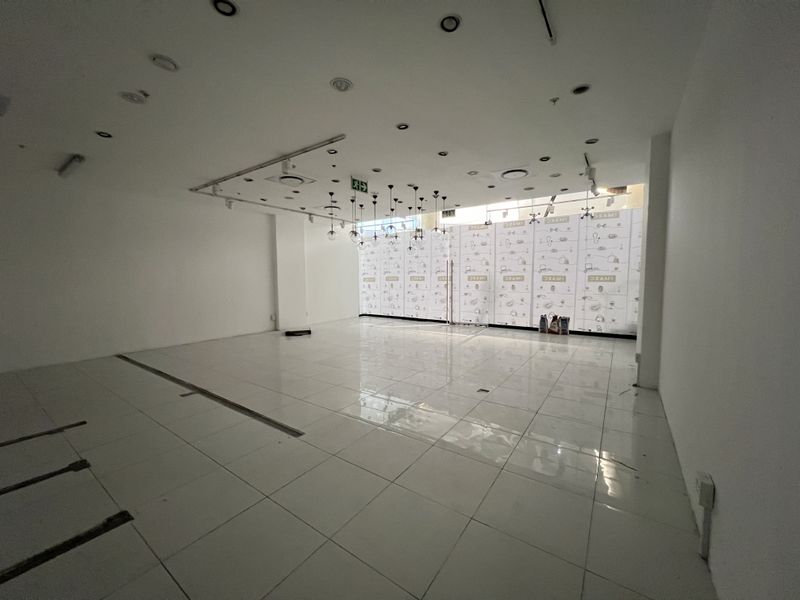 An empty open-plan retail space featuring polished ceramic floor tiles, recessed ceiling lighting, and a large glass storefront with branded window film.