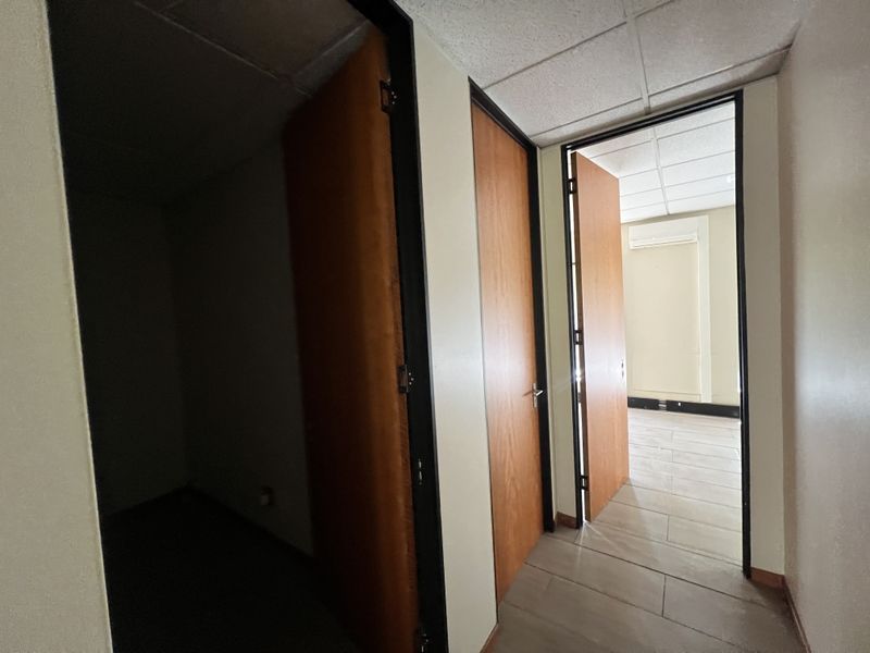 A functional office hallway featuring tiled flooring, suspended ceiling tiles, and multiple wooden doors leading into separate office spaces.