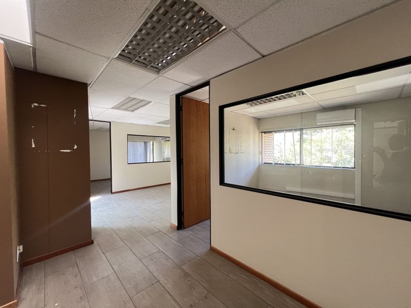 Empty office space featuring suspended ceilings, recessed lighting, glass partitions, and a split-system air conditioning unit, ready for professional fit-out.