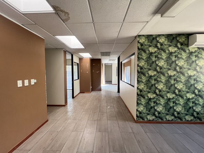 Empty office space featuring tiled flooring, suspended ceilings with recessed lighting, and an integrated air conditioning unit, showing signs of wear and water damage.