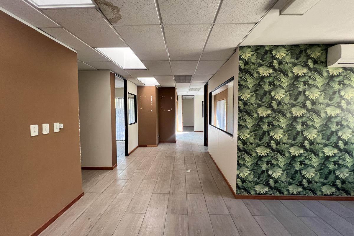 Empty office space featuring tiled flooring, suspended ceilings with recessed lighting, and an integrated air conditioning unit, showing signs of wear and water damage.