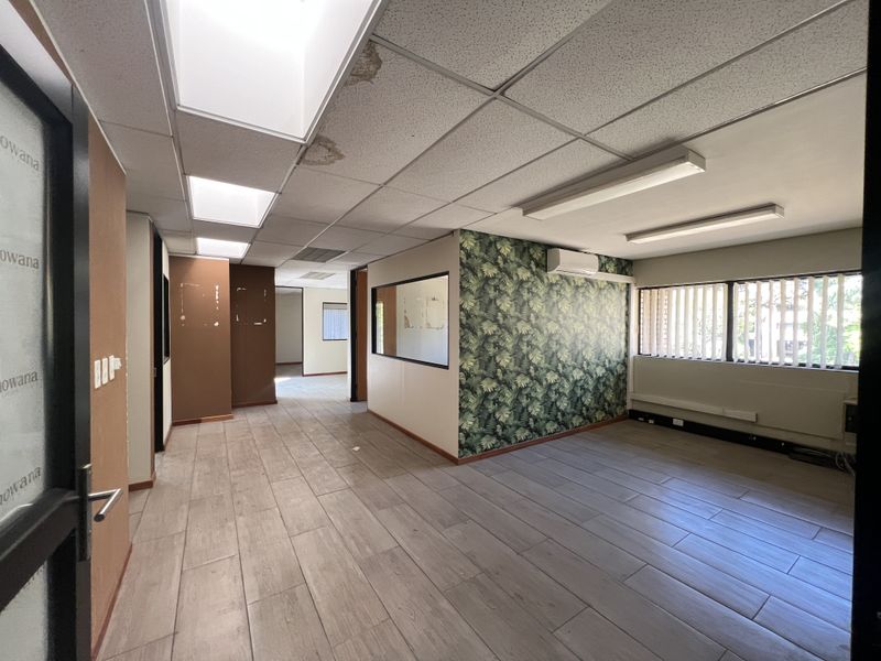 An empty office space featuring tiled flooring, a suspended ceiling with recessed lighting, a split-system air conditioner, and an internal glass partition.