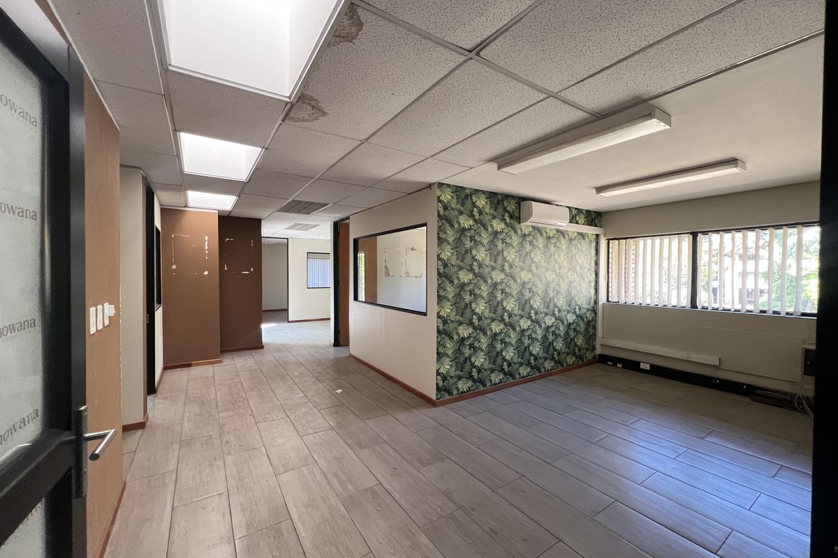 An empty office space featuring tiled flooring, a suspended ceiling with recessed lighting, a split-system air conditioner, and an internal glass partition.