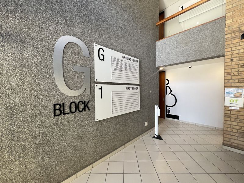 A clean and professional office building entrance lobby featuring a directory board, tiled flooring, and a mezzanine level with a wooden handrail.