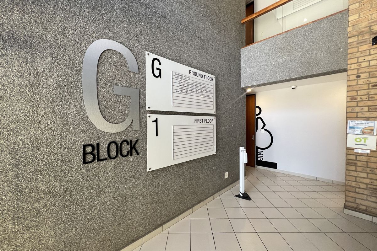 A clean and professional office building entrance lobby featuring a directory board, tiled flooring, and a mezzanine level with a wooden handrail.