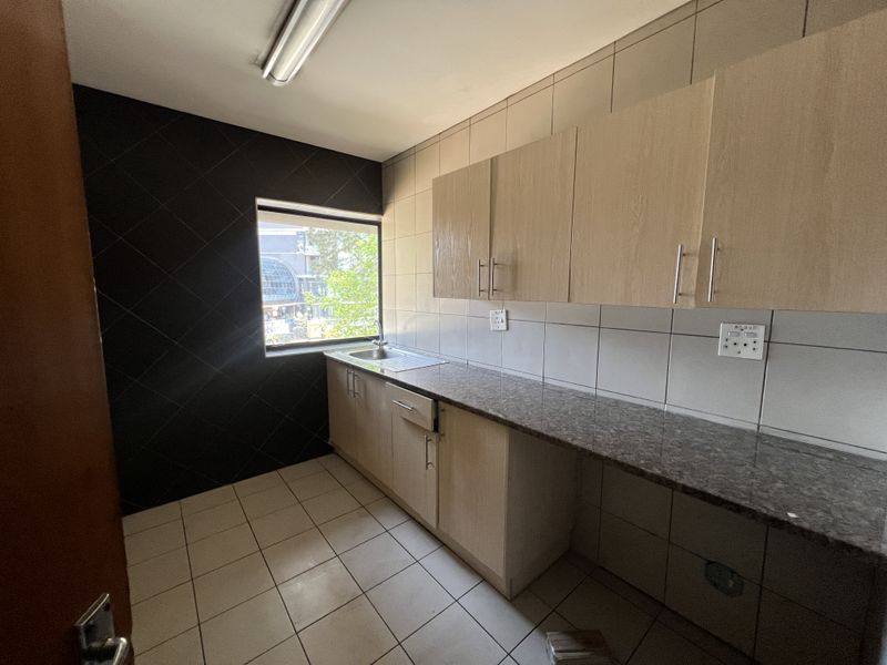 A clean, functional office kitchenette featuring light wood cabinetry, granite countertops, a stainless steel sink, and modern tiled finishes.