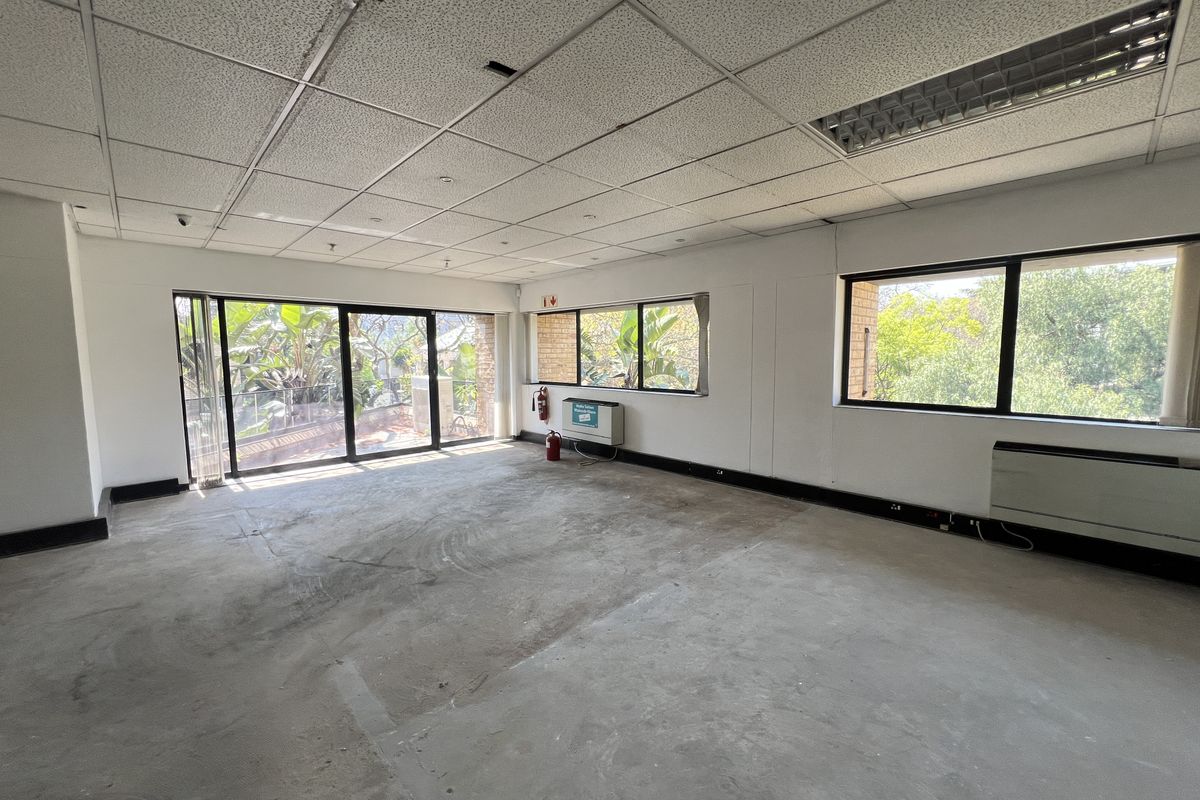 An empty, open-plan office space featuring a suspended ceiling, large windows with natural light, and sliding door access to an outdoor area.