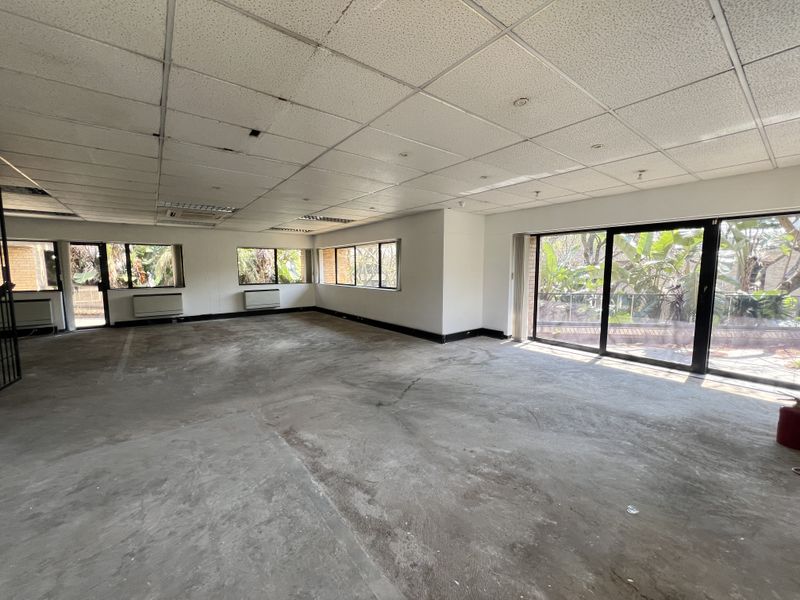 Spacious, empty office suite featuring large windows, sliding glass doors to a balcony, and a suspended ceiling, ready for renovation and custom fit-out.