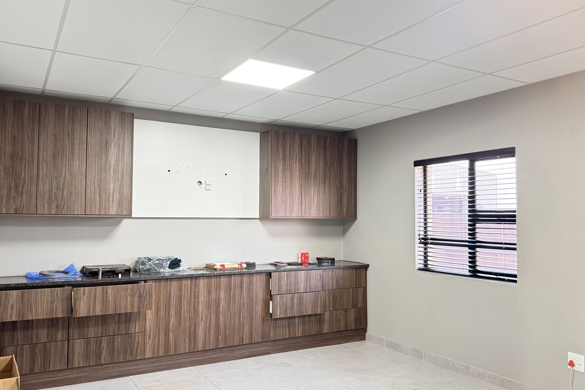 Modern kitchen area featuring wood-grain cabinetry, laminate countertops, and a clean suspended ceiling, offering a functional and well-maintained workspace.