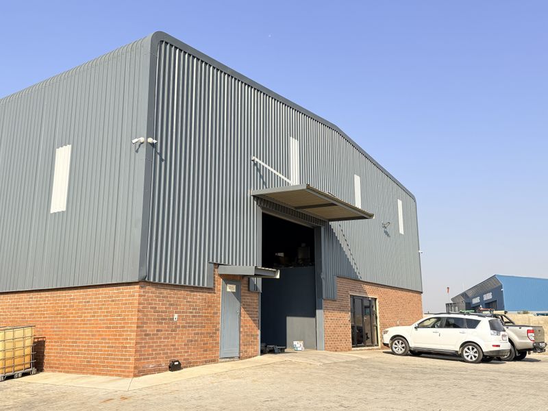 Industrial warehouse building featuring a combination of brick and corrugated metal cladding with a large roller shutter door and paved exterior access area.