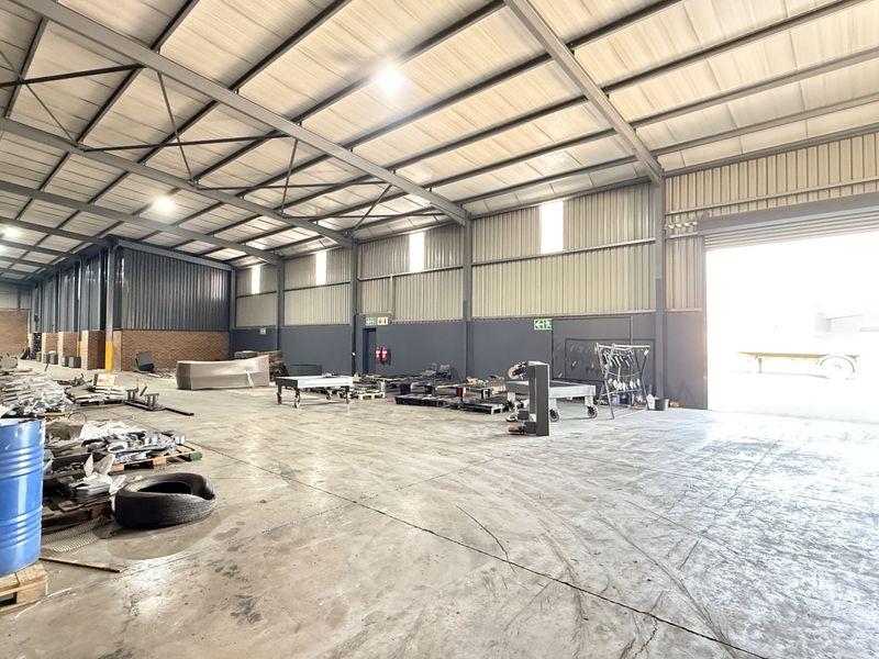 Spacious industrial warehouse featuring a steel portal frame, concrete flooring, high bay lighting, and a large roller shutter door for easy access.