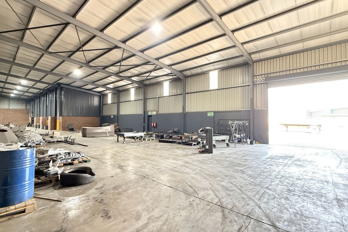 Spacious industrial warehouse featuring a steel portal frame, concrete flooring, high bay lighting, and a large roller shutter door for easy access.