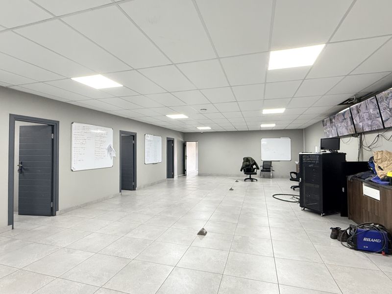 Spacious industrial office area featuring tiled flooring, suspended ceiling with recessed lighting, and a dedicated security monitoring station.