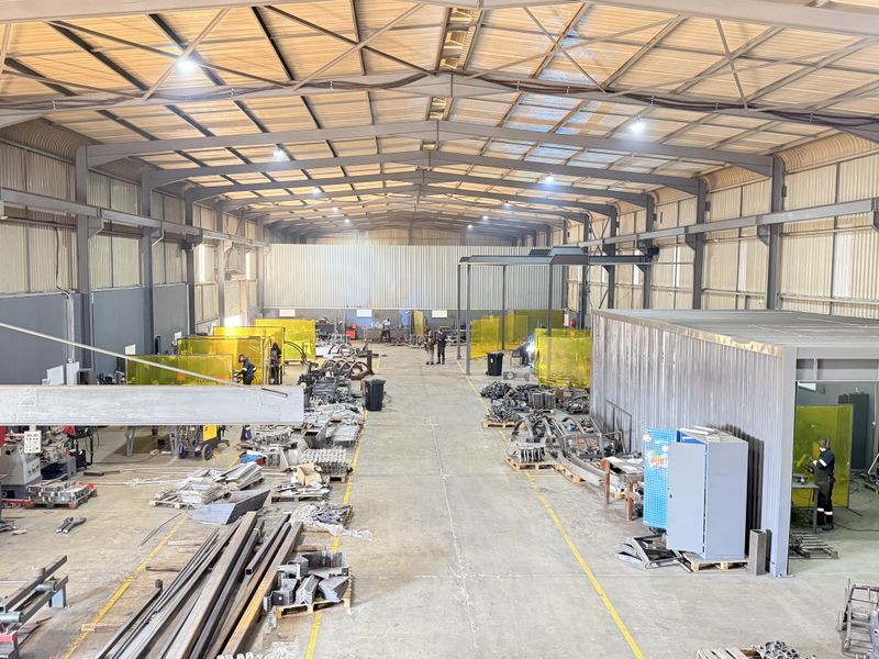 Spacious industrial warehouse featuring a steel portal frame, high-bay lighting, concrete flooring, and dedicated partitioned welding bays for manufacturing operations.