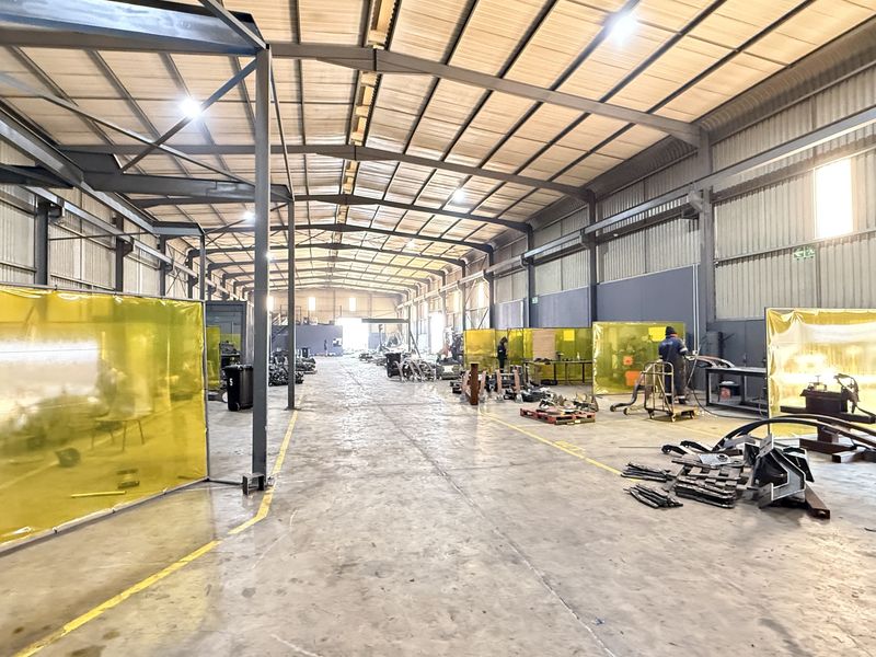 Spacious industrial warehouse facility featuring a steel portal frame structure, concrete flooring, and high-bay lighting, currently utilized for metal fabrication and welding operations.