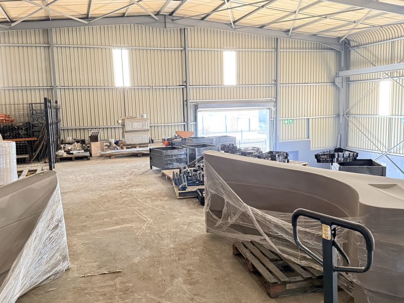 Spacious industrial warehouse unit featuring high ceilings, corrugated metal walls, concrete flooring, and large roller shutter access.