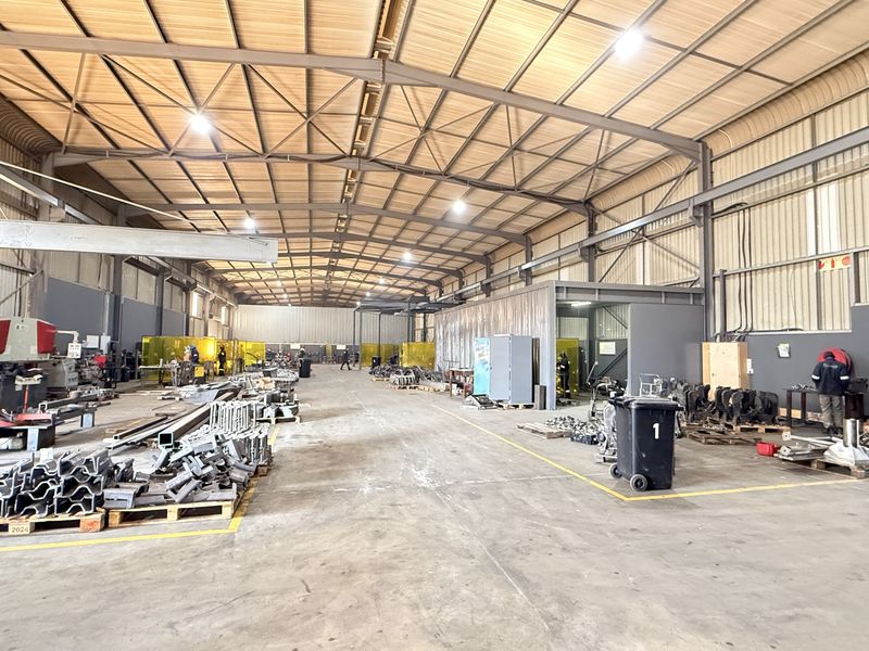 Spacious industrial warehouse featuring a high-clearance steel portal frame, concrete flooring, and functional metal cladding, suitable for manufacturing or storage operations.