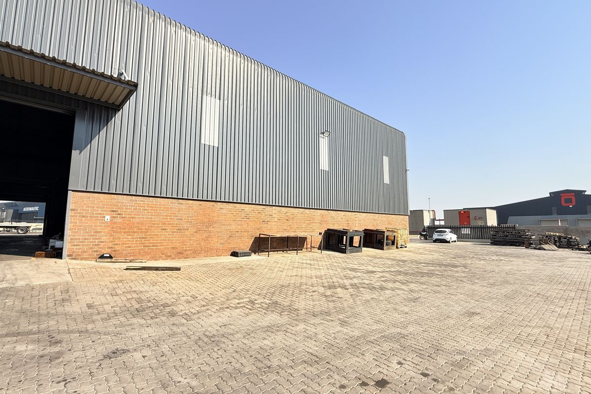 Industrial property exterior featuring a large corrugated metal warehouse structure, brick base, and extensive paved yard area suitable for logistics or storage.