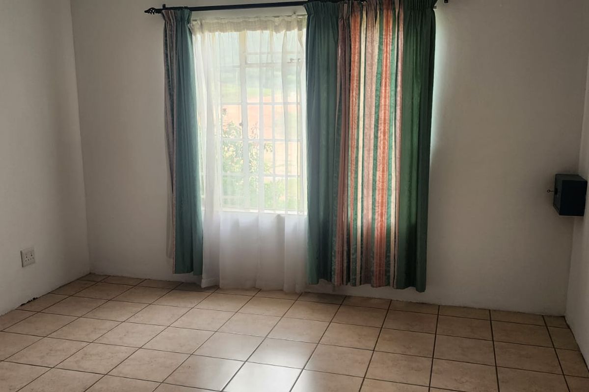 A simple, empty bedroom featuring tiled flooring and a window fitted with security bars, providing a neutral space ready for personalization.