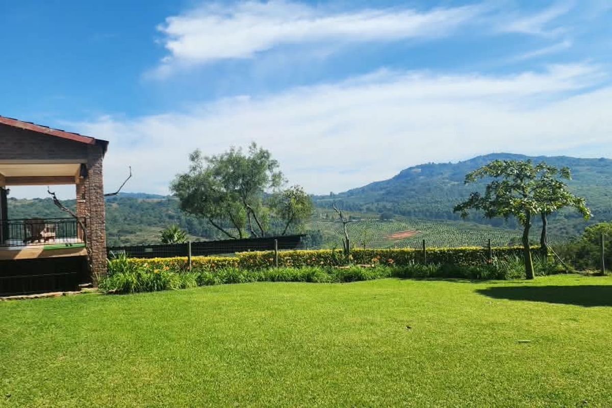 A well-maintained rear garden featuring a covered patio, brick exterior, and expansive views of the surrounding hills and agricultural landscape.