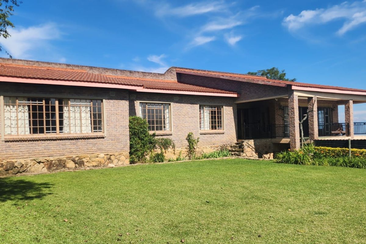 A well-maintained brick farmhouse featuring a tiled roof, stone foundation, and a spacious covered patio overlooking a large green lawn.
