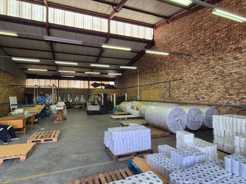 Spacious industrial warehouse featuring exposed brick walls, high steel truss ceilings, concrete flooring, and a roller shutter door for efficient access.