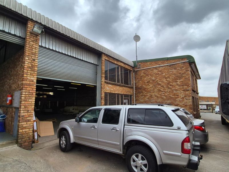 Industrial property exterior featuring a large roller shutter door, brick facade, and metal roofing, suitable for warehouse or workshop operations.