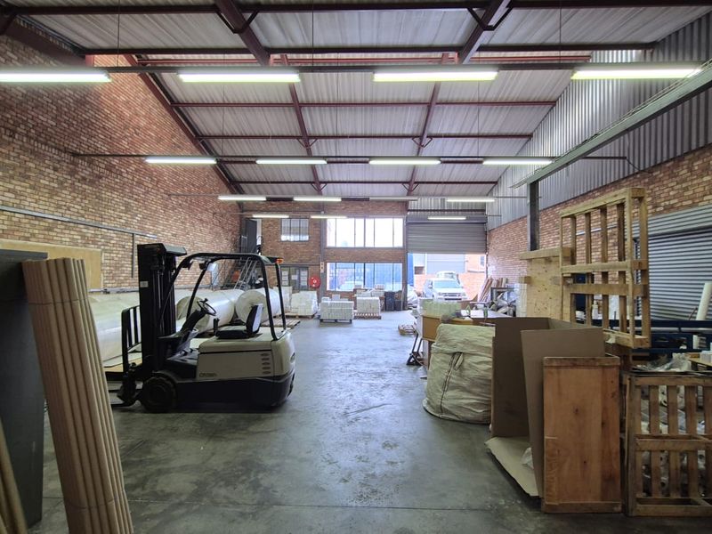 Spacious industrial warehouse unit featuring exposed brick walls, high steel truss ceilings, concrete flooring, and a large roller shutter door for easy access.