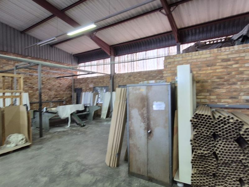 Industrial utility space featuring exposed brick walls, steel roof trusses, and concrete flooring, suitable for workshop or storage use.