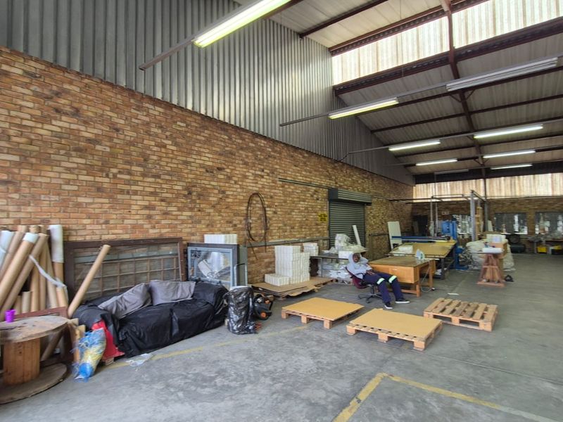 Spacious industrial utility area featuring exposed brick walls, high corrugated metal roofing, concrete flooring, and functional fluorescent strip lighting.