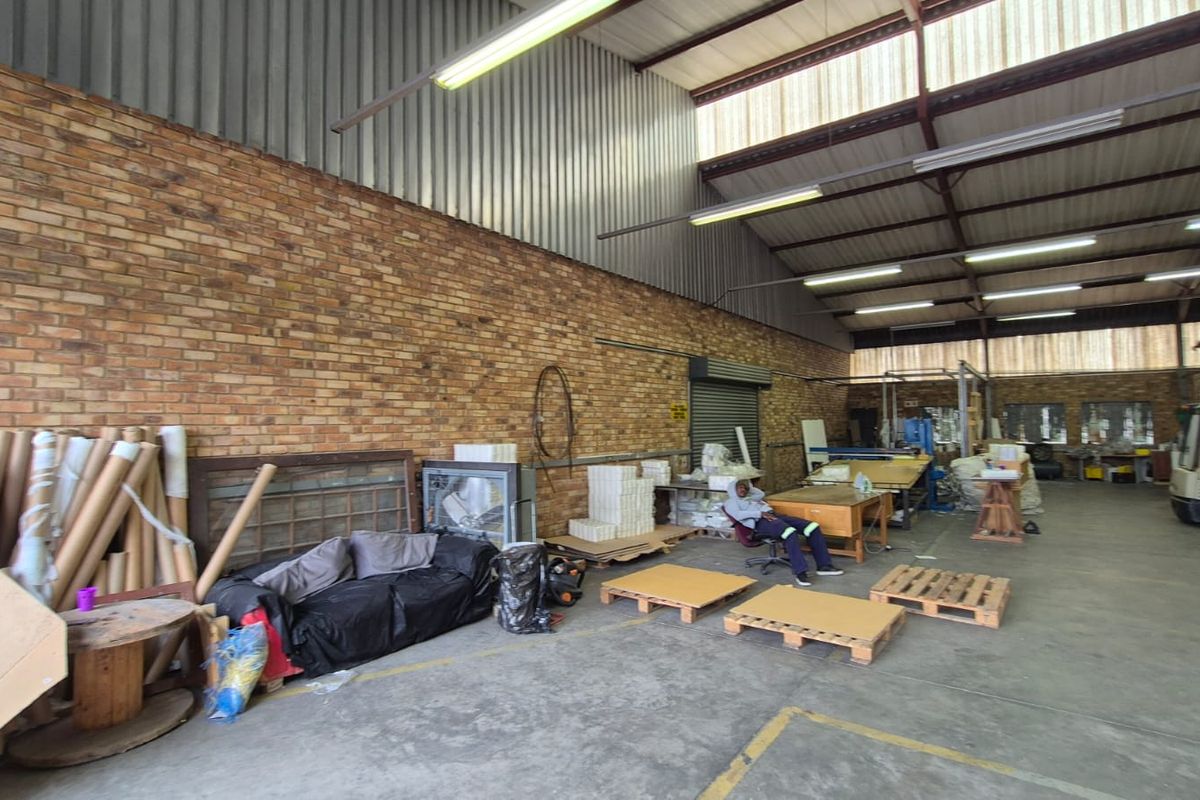 Spacious industrial utility area featuring exposed brick walls, high corrugated metal roofing, concrete flooring, and functional fluorescent strip lighting.