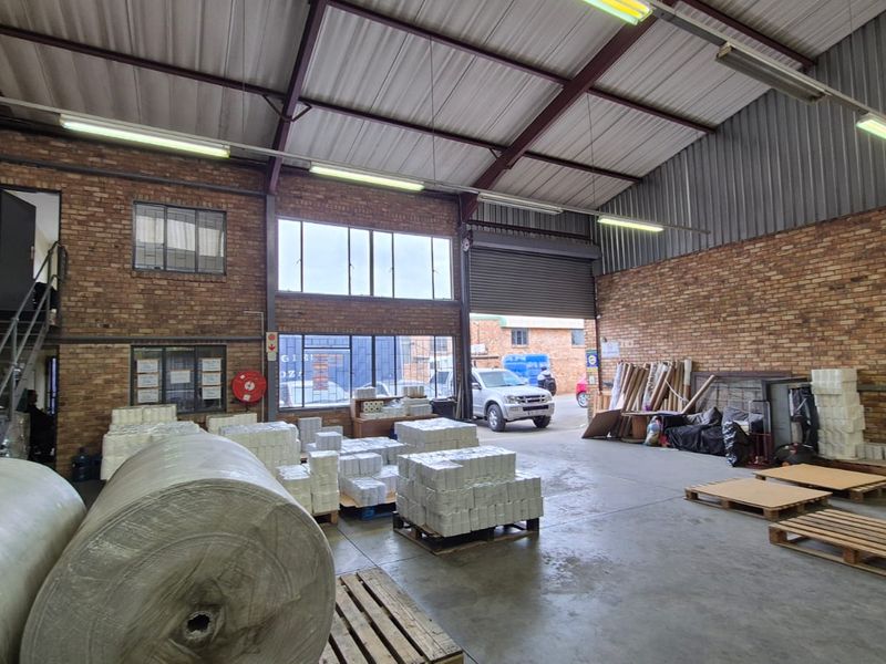 Spacious industrial warehouse unit featuring exposed brick walls, high-clearance metal roofing, concrete flooring, and a large roller shutter door for easy access.